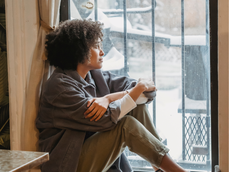 woman sitting on window sill, feeling alone after her abortion, hoping for support