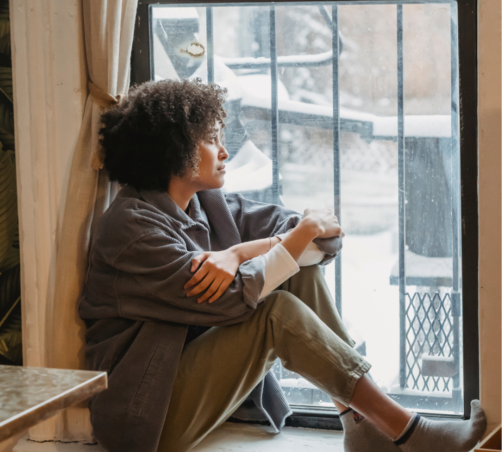 woman sitting on window sill, feeling alone after her abortion, hoping for support