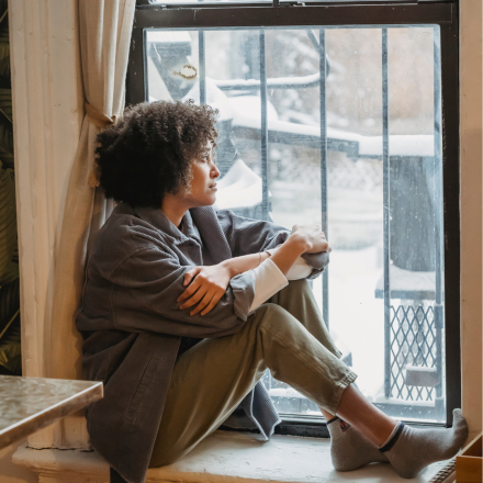 woman sitting on window sill, feeling alone after her abortion, hoping for support