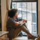 woman sitting on window sill, feeling alone after her abortion, hoping for support